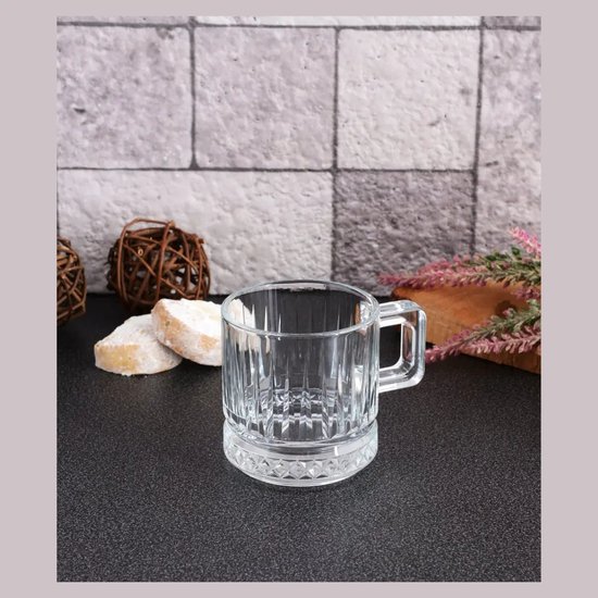 Een leeg, doorzichtig glazen theeglas met een gedessineerde bodem en een handvat.