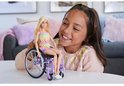 Een meisje houdt Barbie, die in een rolstoel zit, vast. Barbie draagt een gekleurd geruit jumpsuit.
