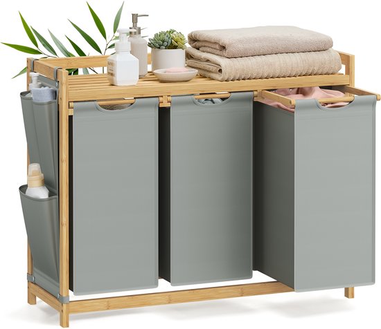 Panier à linge gris à 3 compartiments en bambou, rempli de linge et avec des savons et serviettes sur l'étagère.