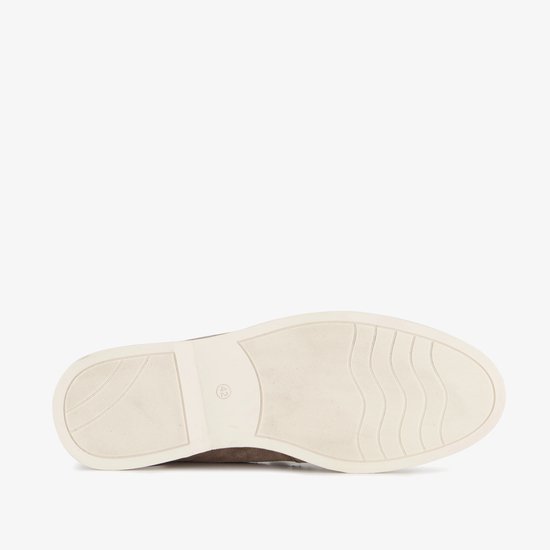 De onderkant van een bruine suède loafer met een beige zool met golfpatroon.
