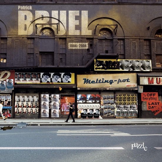 Albumcover 'Puzzle' van Patrick Bruel. Een straatbeeld met een gebouw met de naam Patrick Bruel erop. Op de etalages staan posters van Patrick Bruel.