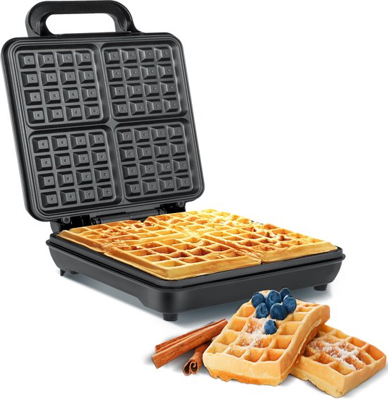 Open zwart wafelijzer met vier goudbruine wafels, bestrooid met poedersuiker en gegarneerd met blauwe bessen en kaneelstokjes.