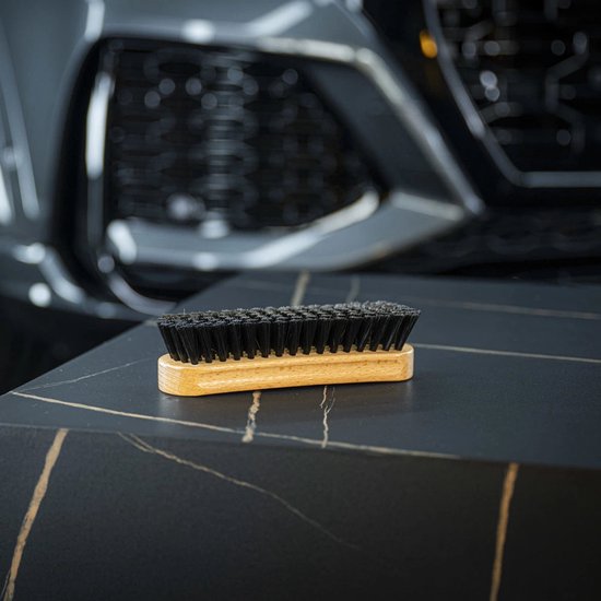 Brosse de nettoyage textile à manche en bois et poils noirs, sur une surface sombre polie.
