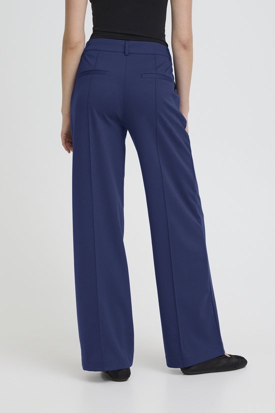 Model van achteren gezien in een donkerblauwe, wijde broek met rechte pijpen en een hoge taille.