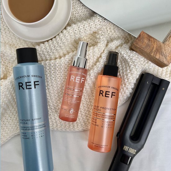 Drie REF-producten: een blauwe textuurspray, een roze shine elixir en een oranje hittebeschermingsspray, naast een krultang.