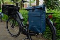 Zwarte e-bike met een blauwe rolltop fietstas/rugzak van Voltano op de bagagedrager. Met zwarte krat voorop.