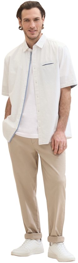 Model draagt een wit kortarmig overhemd met subtiel patroon, borstzakje met blauwe rand, over een wit T-shirt.