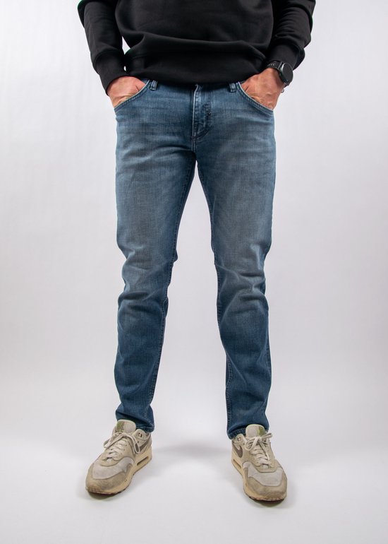 Homme en jean bleu coupe fuselée, sweat noir et baskets beiges.