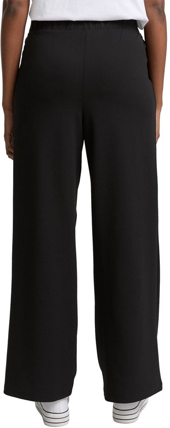 Achterkant van een zwarte wijde broek met witte sneakers.