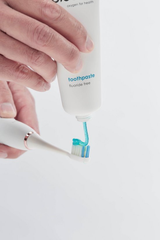 Hand spuit blauwe tandpasta op een witte elektrische tandenborstel uit een witte tube.