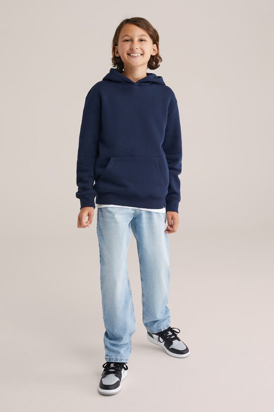 Jongen in een donkerblauwe hoodie en lichtblauwe jeans, lachend naar de camera.
