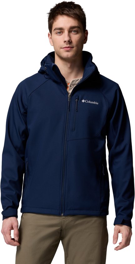 Man in een donkerblauwe Columbia softshell jas met capuchon, een rits aan de voorkant en zakken. Draagt een beige shirt en een bruine broek.