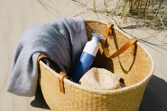 Blauwe Dopper drinkfles in een rieten mand met een handdoek en strooien hoed.