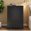 Commode noire à 5 tiroirs, avec des livres, un réveil et une lampe sur le dessus.