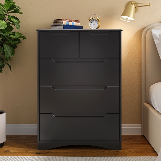 Commode noire à 5 tiroirs, avec des livres, un réveil et une lampe sur le dessus.
