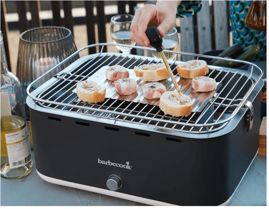 Hand met een kwastje die broodjes met spek op een grijze tafelbarbecue besmeert.