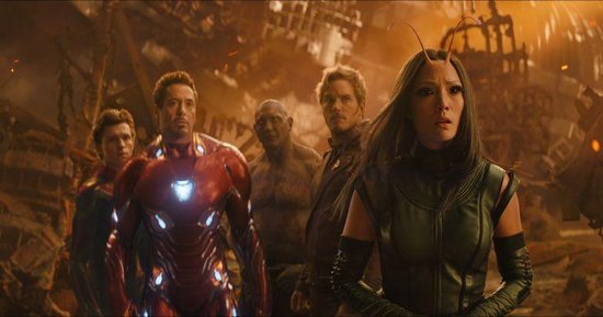 Een groep van vijf Avengers, waaronder Iron Man, Mantis, Star-Lord en Spider-Man, staat in een verwoeste stad.