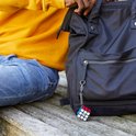 Rubik's Cube sleutelhanger bevestigd aan een zwarte tas, gedragen door iemand met een gele trui en spijkerbroek.