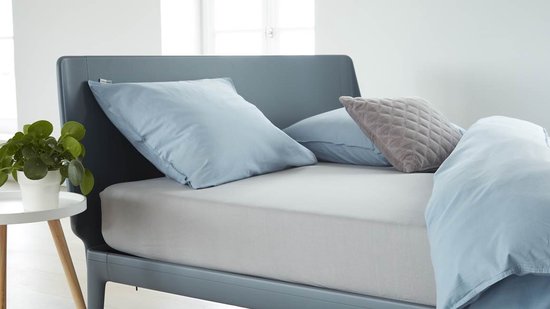 Bed opgemaakt met een lichtgrijs hoeslaken, lichtblauwe kussens en dekbed.