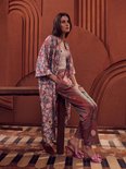 Vrouw zittend in een gedessineerde kimono met paarse broek, beide met bloemen- en vogelprint.