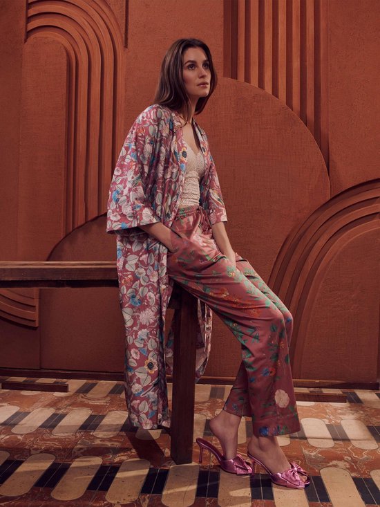 Vrouw zittend in een gedessineerde kimono met paarse broek, beide met bloemen- en vogelprint.