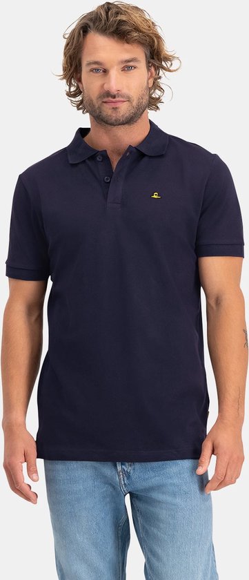 Man met kort blond haar, kijkend naar voren, draagt een donkerblauw NOMAD poloshirt en spijkerbroek.
