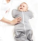 Baby in grijze Love to Dream™ Swaddle Up™ met witte strepen, armen omhoog, met een hand op de buik.
