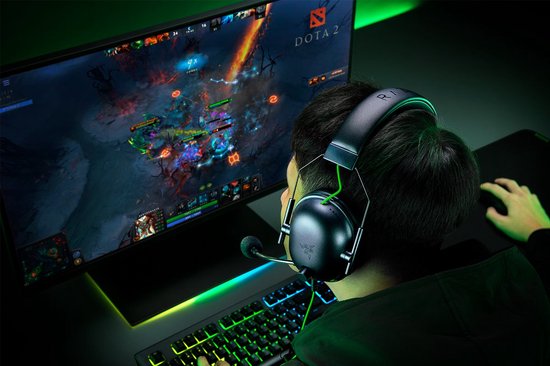 Speler met een Razer gaming headset, kijkend naar een Dota 2 wedstrijd op een monitor.