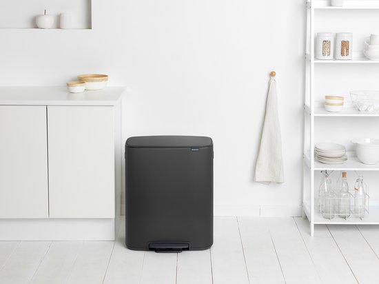 Donkergrijze Brabantia prullenbak met een gebogen bovenrand en een voetpedaal.