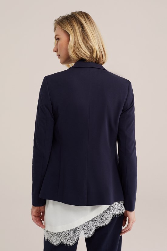 Dames donkerblauwe blazer, van achteren gezien, met een witte top met kanten rand.