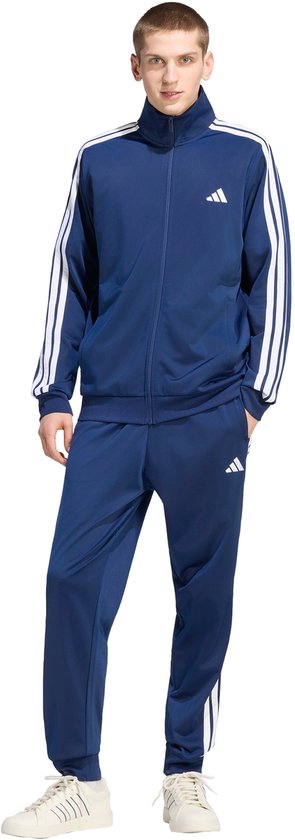 Man, vooraanzicht, donkerblauw trainingspak met witte Adidas strepen op mouwen en pijpen.