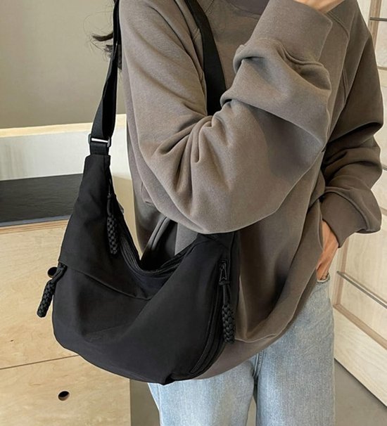 Zwarte crossbody tas, gedragen over de schouder, met een centrale ritssluiting.