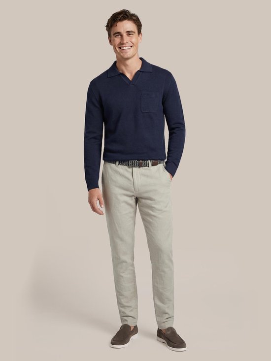 Man in een beige linnen broek en donkerblauwe polo, met een riem en bruine instappers.
