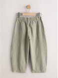 Lichtgroene broek met verticale textuur en elastische taille, hangend aan een kledinghanger.
