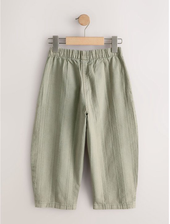 Lichtgroene broek met verticale textuur en elastische taille, hangend aan een kledinghanger.