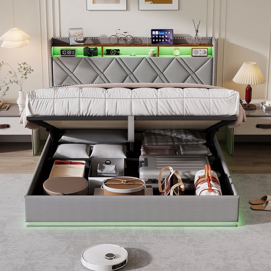 Grijs bed met opengewerkte opbergruimte, gevuld met koffers en textiel, en voorzien van groene LED-verlichting.