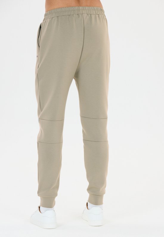 Achterkant van beige trainingsbroek met paneeldetails op de benen, met witte sneakers.