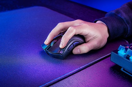Een hand met een donkergrijs gamingmuis, met een scrollwiel en knoppen, op een zwart gamingmuismat.