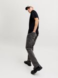 Man met pet, draagt zwart T-shirt en donkergrijze jeans met zwarte schoenen.