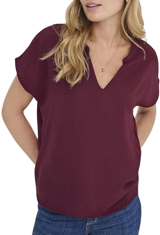 Model met donkerrode blouse met korte vleermuismouwen, V-hals, en jeans.