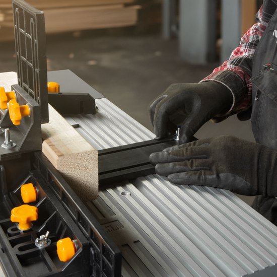 Handen met zwarte handschoenen stellen een zwarte geleiderail in op een grijze tafel met ribbels.