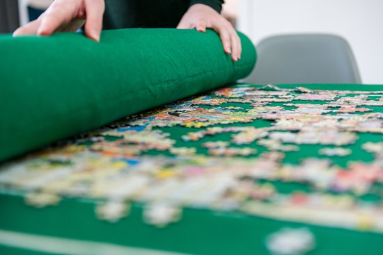 Vrouw rolt een groene puzzelmat met een gedeeltelijk gelegde puzzel erop op.
