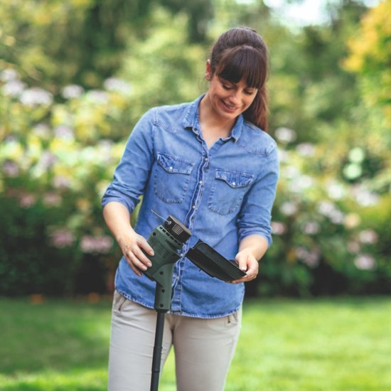 Vrouw met sproeten in een spijkerblouse monteert een onderdeel aan de groene Bosch grastrimmer.