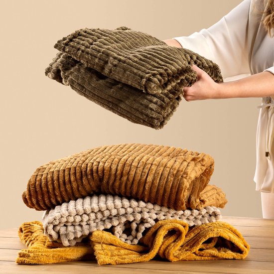 Stapel van pluizige plaids in verschillende kleuren waaronder bruin, olijfgroen en geel.