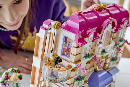 Meisje bouwt LEGO Friends Grand Hotel met paars dak en balkon met poppetjes.