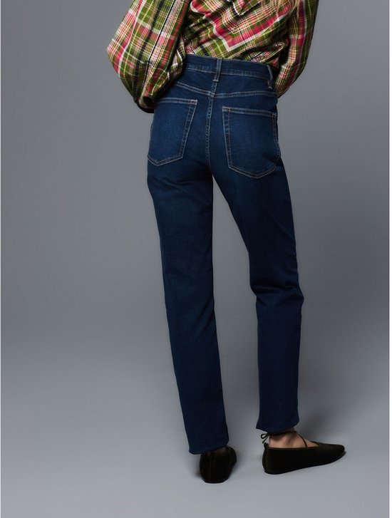 Dames met donkerblauwe jeans, beige, rood en groen geruite blouse.