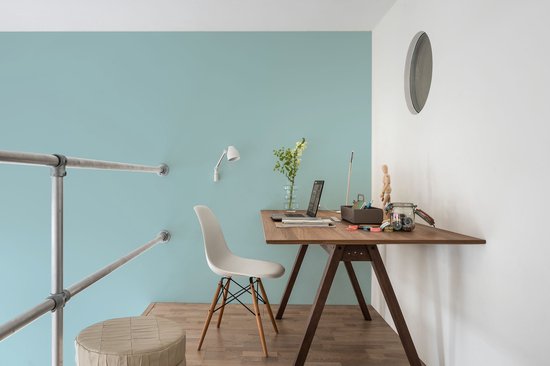 Bureauhoek met lichtblauwe muur, houten bureau, witte stoel en laptop.