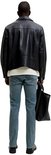Achterkant van een man in blauwe slim fit jeans, zwarte jas en met een zwarte tas.