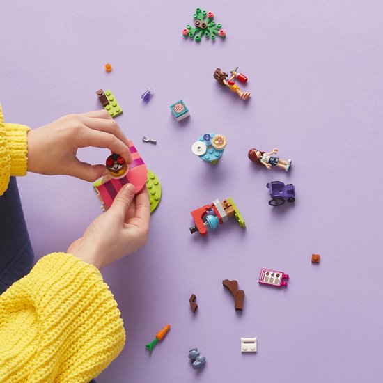 Mains d'enfant construisant La Crêperie LEGO Friends avec des pièces détachées sur fond violet.
