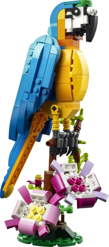 Een gedetailleerde, gele en blauwe LEGO papegaai op een bruine tak met roze bloemen op een groene ondergrond.